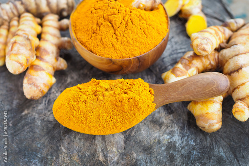 Turmeric powder and fresh turmeric in wooden spoon on old wooden table. Herbs are native to Southeast Asia.