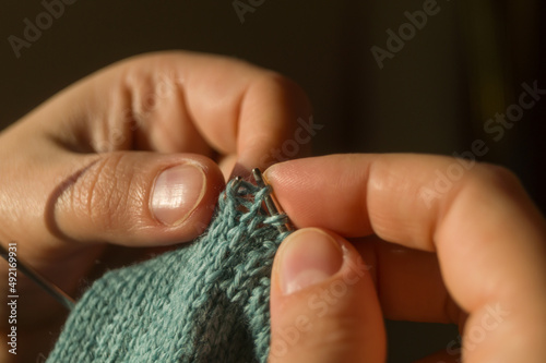 Close-up hand knitting. Hobbies, handicrafts. Knitting warm clothes from woolen fine yarn by hand on metal needles. Selective focus