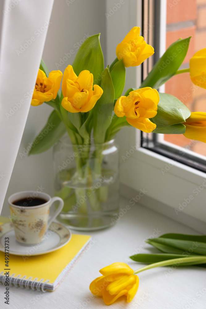 Yellow tulips in a jar, a cup of coffee and a notebook on the windowsill Yellow tulips in a jar, a cup of coffee and a notebook on the windowsill