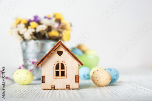 Happy Easter greeting card. Miniature wooden house. Rabbits, colorful eggs, spring flowers with tag for text..
