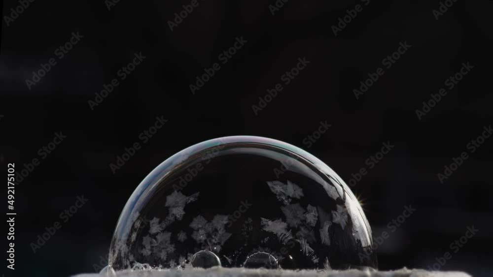 Festive winter background with air balloon ice pattern. A soap bubble lies on the snow on a black background, snowflakes fall on it and freeze.