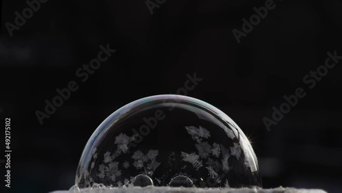 Festive winter background with air balloon ice pattern. A soap bubble lies on the snow on a black background, snowflakes fall on it and freeze.