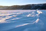 Ice hummocks on Baikal Lake in a sunny day. Winter landscape with beautiful transparent ice floes on foreground.