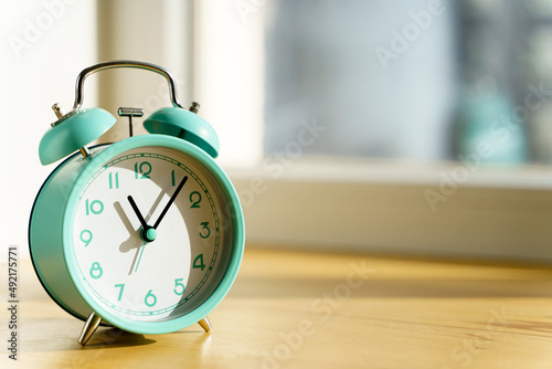 Alarm clock in the morning on the table in the bedroom against the background of the window with the morning bright sun. Wake up, time, new day, optimism concept