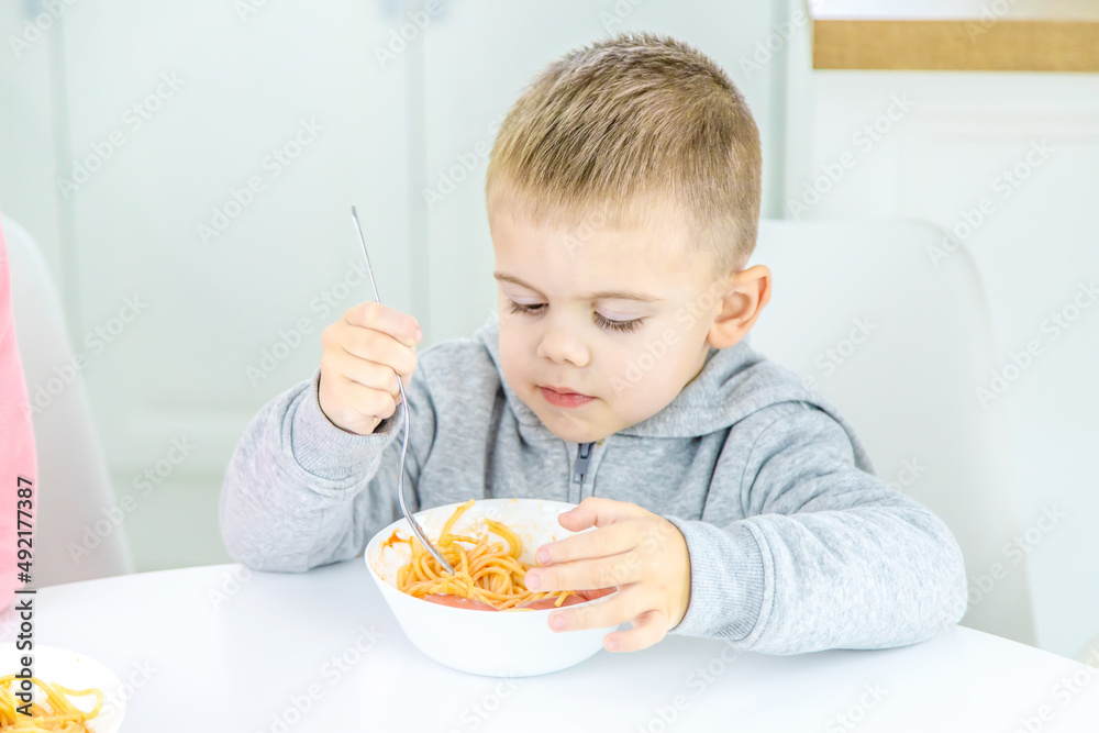 children in the kitchen at the table eat pasta. children in the kitchen at the table eat pasta.