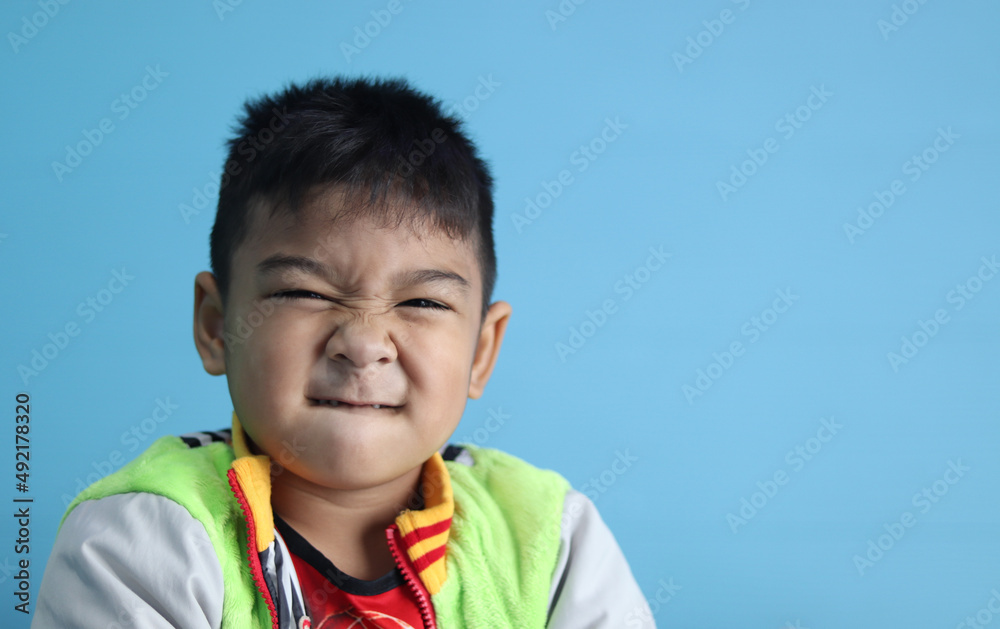 Asian boy, 6 years old, short black hair, sees face, eyes, nose, mouth closed, smiling without teeth. Eyes slightly closed, cute, bright, looking at camera, happy to take pictures, blue background