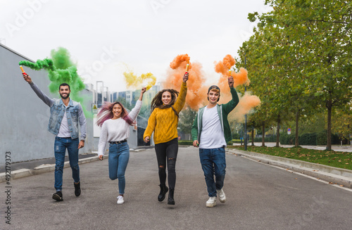 Group of young students bonding outdoors  happy cheerful people having party and running with colored smoke bombs
