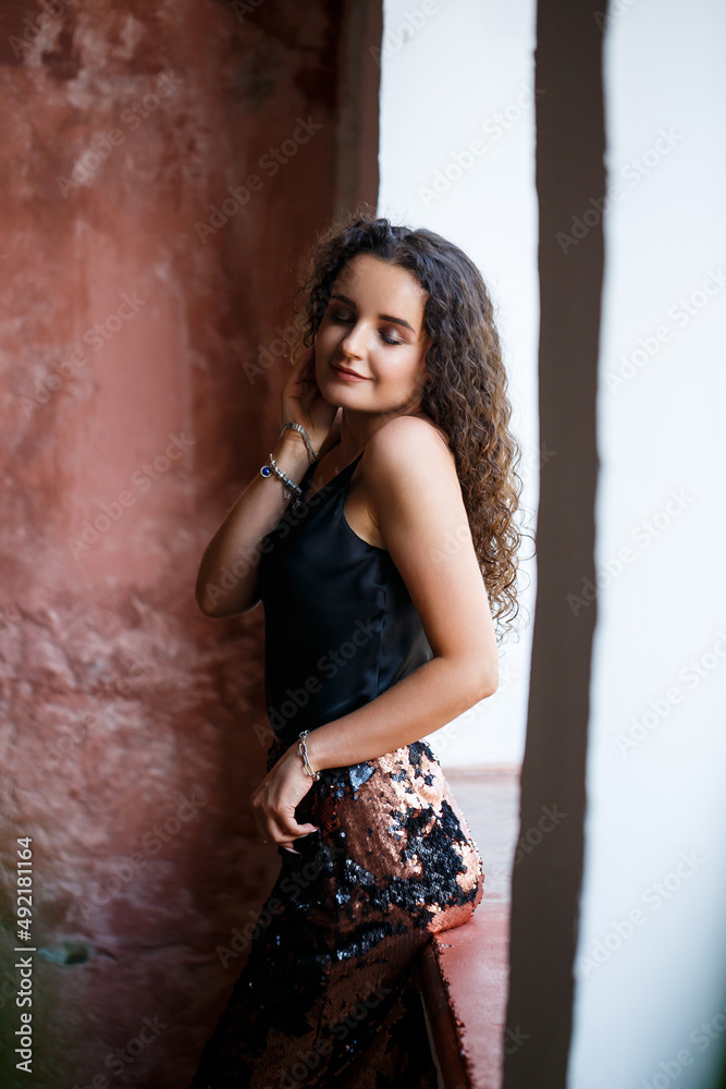 Fototapeta premium Portrait of a young charming woman with curly hair, fair-skinned girl in a black top and with a smile on her face. Curly woman in light clothes