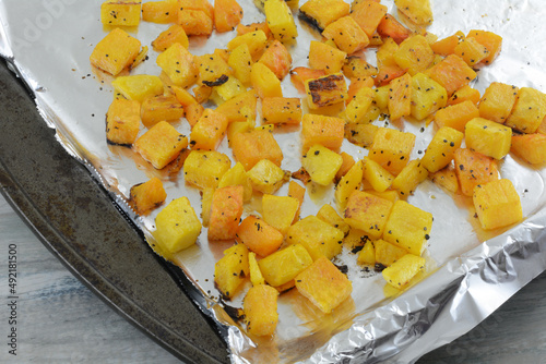 Roasted butternut squash cubes with spices on aluminum foil lined baking sheet