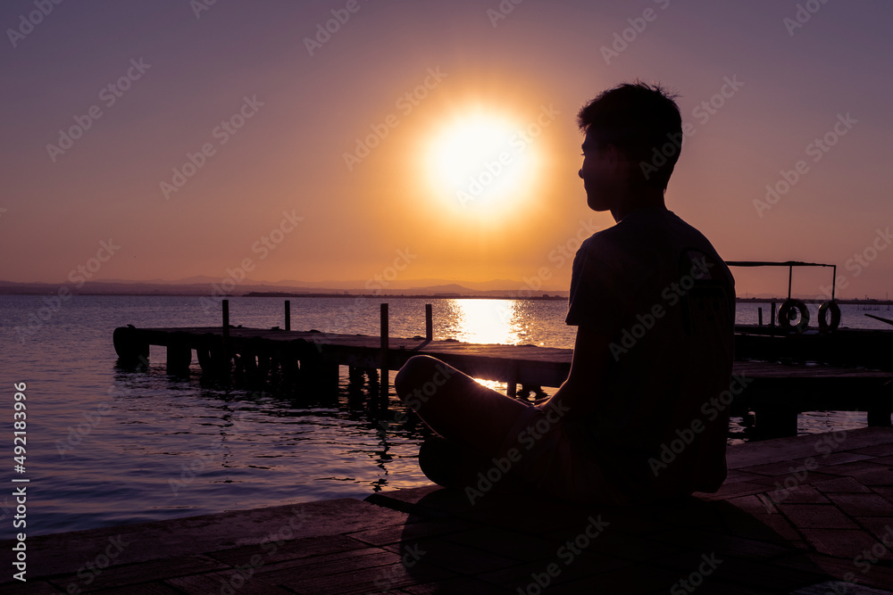 Hombre joven sentado en el muelle al atardecer. Relajación. Meditación.