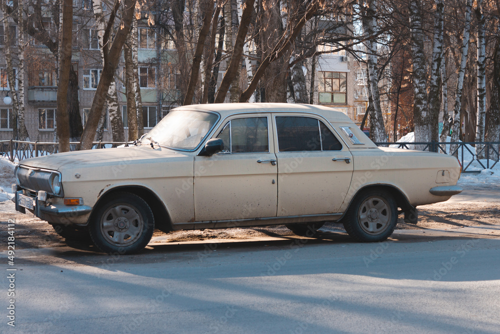An old russian car - Volga Gaz 2410 - parked on the street against trees and residential building in the city An old russian car - Volga Gaz 2410 - parked on the street against trees and residential building in the city