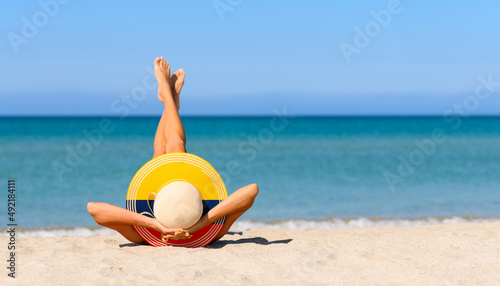 Fototapeta Naklejka Na Ścianę i Meble -  A slender girl on the beach in a straw hat in the colors of the Colombian flag. The concept of a perfect vacation in a resort in the Colombia. Focus on the hat.