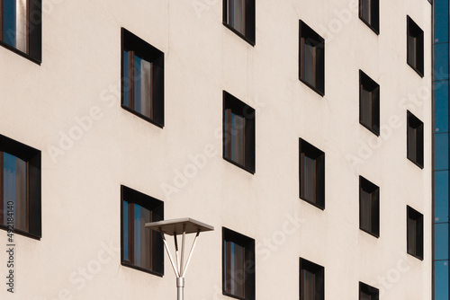 A beige building with lots of black windows. A street lamp is on the foreground. Side view minimalistic picture