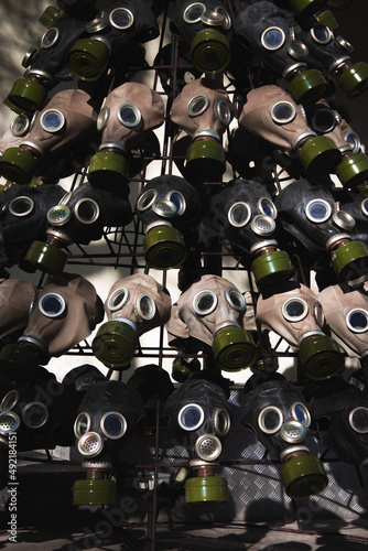 A full frame dark image of rows of gas masks with bright green filters on them and blue glass eyepieces photo