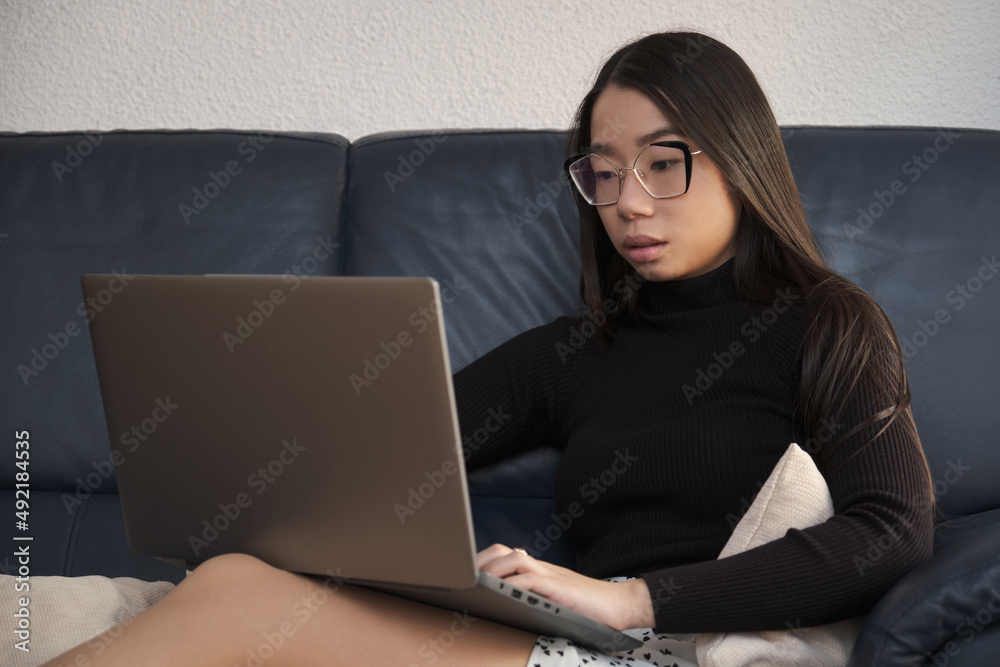 Young asian woman working on the laptop sitting on the sofa. Young asian woman working on the laptop sitting on the sofa.