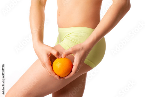 A young woman holds an orange citrus on a white background. The concept of cellulite problem