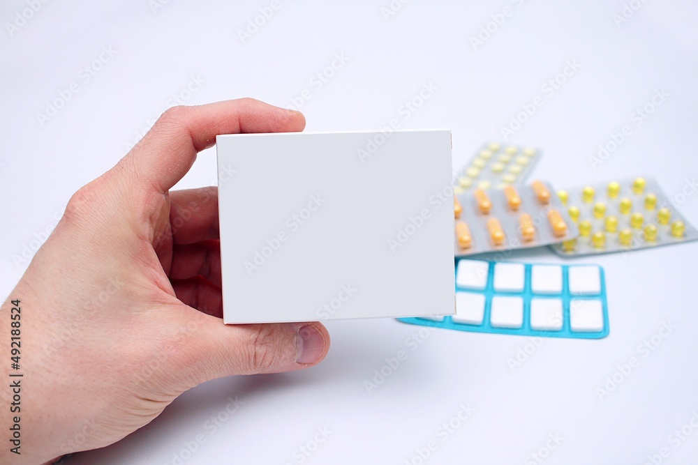 Pudełko prostokątne z lekiem trzymane w ręku mężczyzny na tle innych leków i na białym tle - obrazy, fototapety, plakaty 