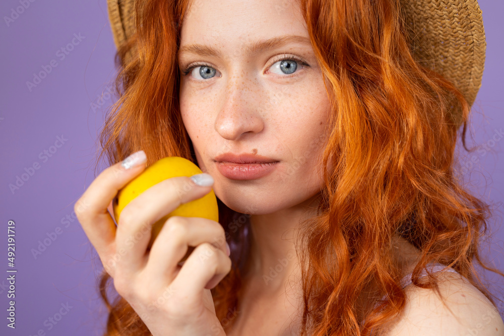 Portrait of a beautiful redhair young woman with blue eyes and freckles in a straw hat holding an apple closed to her face. Portrait of a beautiful redhair young woman with blue eyes and freckles in a straw hat holding an apple closed to her face.