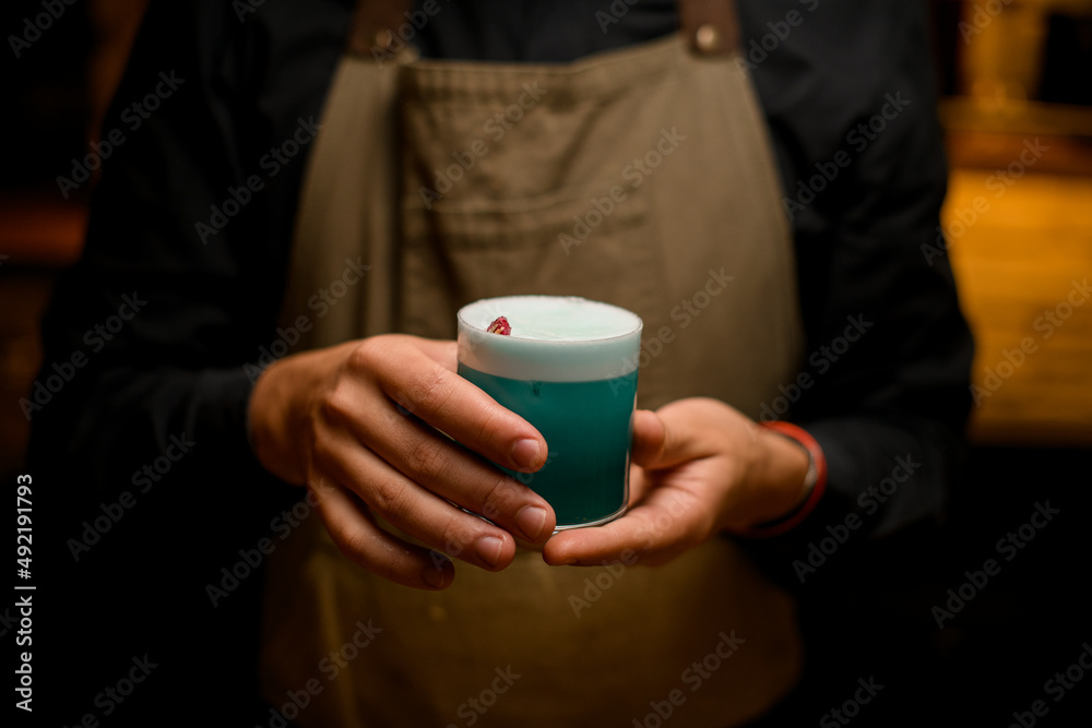 hands of bartender gently holds glass with blue foamy alcoholic drink hands of bartender gently holds glass with blue foamy alcoholic drink