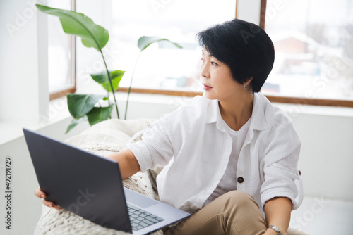  woman freelancer connecting to the Internet from home. The adorable asian woman using a laptop, in a stylish living room,