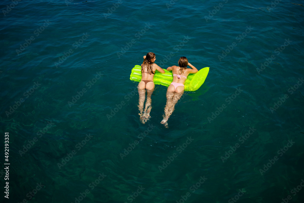 Two women on an inflatable mattress swim in the mediterranean sea, vacation by the sea