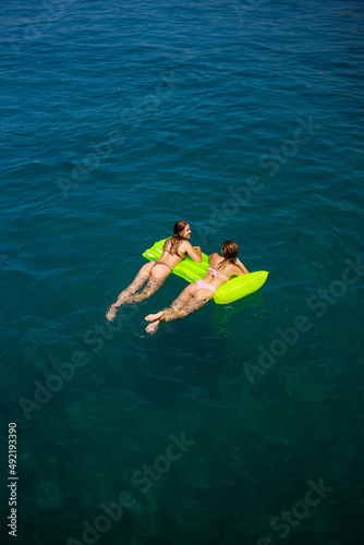 Two women on an inflatable mattress swim in the mediterranean sea, vacation by the sea