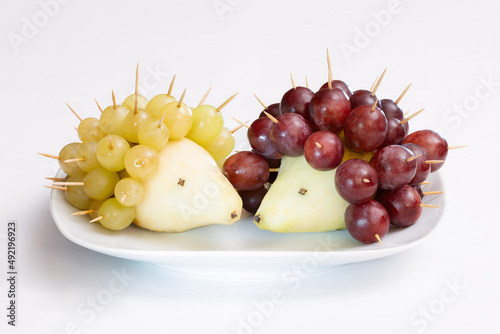 Hedgehogs made of fruits. Pear and grapes on a plate.