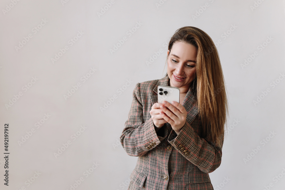 Portrait of a smiling millennial business woman working online looking into a phone typing using wireless technology and a smartphone on a white isolated background. Selective focus