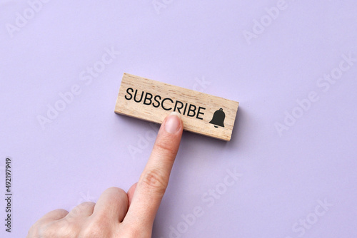 A wooden plate and a bell icon with the inscription subscribe in it. Internet channel subscription symbol and subscription reminder