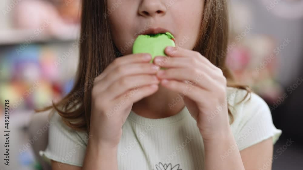 Close up front view, unrecognizable kid brunette girl with big smile and white healthy teeth bites pistachio macaron cookie. Tasty sweet color macaron