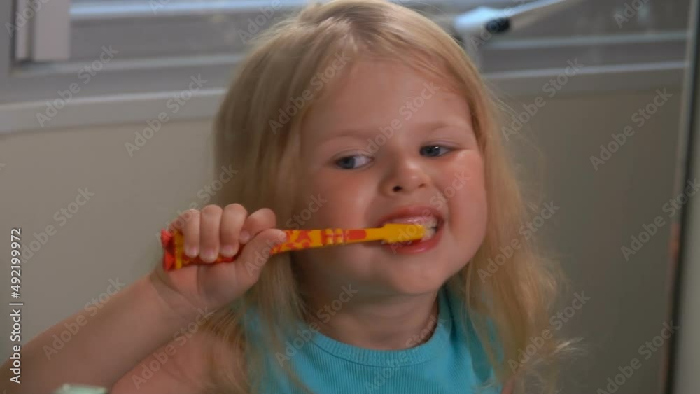 Close-up of the little blond girl brushing her teeth with an orange toothbrush Close-up of the little blond girl brushing her teeth with an orange toothbrush