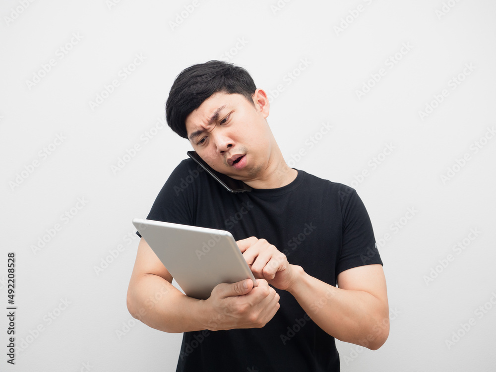 Asian man using tablet with talking mobile phone busy and serious emotion Asian man using tablet with talking mobile phone busy and serious emotion
