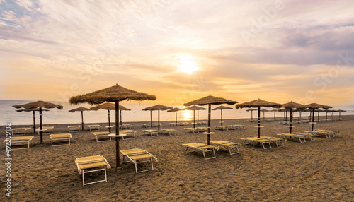  empty beach during beautiful sunrise or sunset with chaise loungues and nice umbrellas with blue sea  sun glow and amazing cloudy sky on thr background