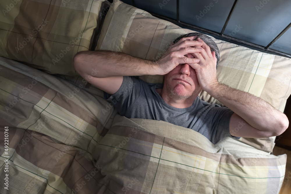 Man with insomnia lying in bed and snorting from exhaustion. Man with insomnia lying in bed and snorting from exhaustion.