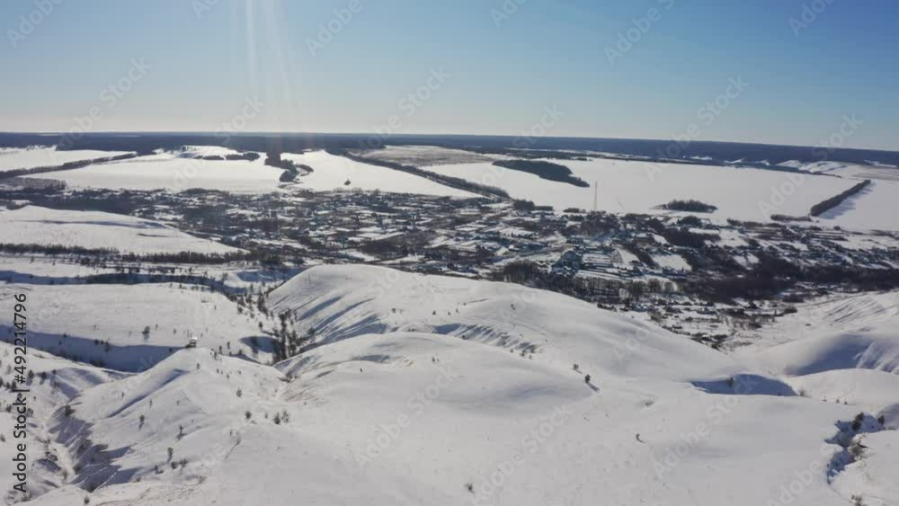 The village appears from behind the snowy mountains on a bright sunny day. View. from the air The village appears from behind the snowy mountains on a bright sunny day. View. from the air