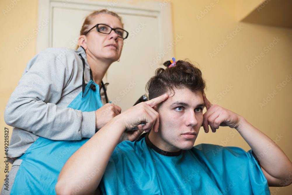 Fototapeta premium Teen guy shows mom who cuts his hair which he wants hairstyle. Mom cuts her teen son's hair, at the same time they communicate and laugh