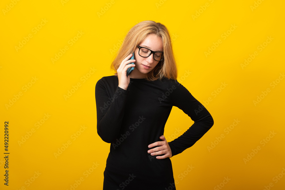 Sad young woman blonde, in glasses, dressed in black dress, talking on phone, on a yellow background. Sad young woman blonde, in glasses, dressed in black dress, talking on phone, on a yellow background.