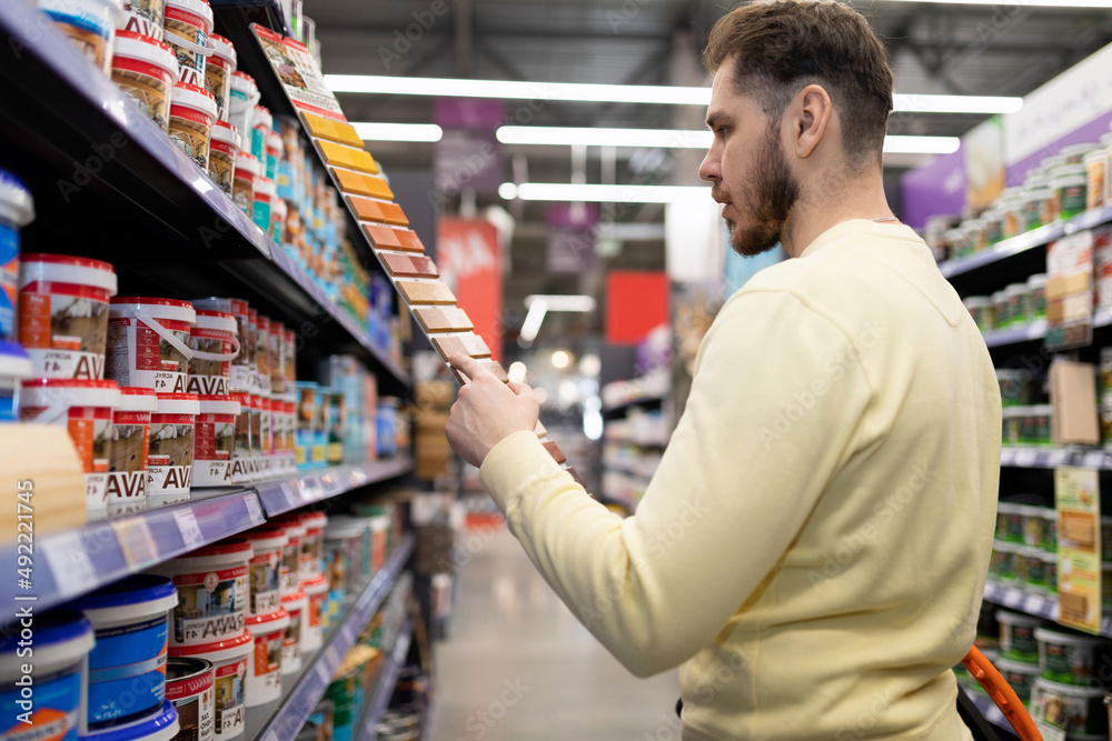 a male buyer in a hardware store chooses paint for interior and exterior painting work a male buyer in a hardware store chooses paint for interior and exterior painting work