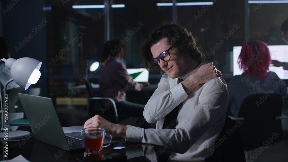 Businessman overwork and suffer from pain in neck sitting at desk in dark office Businessman overwork and suffer from pain in neck sitting at desk in dark office
