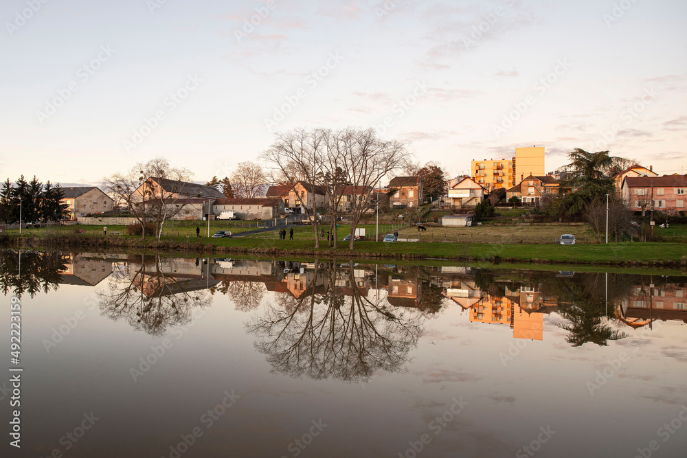 Sunset on a lake in Burgundy, France, with trees in winter and houses and buildings behind