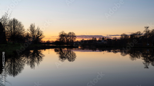 Sunset on a lake in Burgundy in France, with the black silhouettes of trees in winter