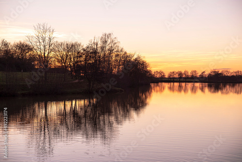 Sunset on a lake in Burgundy in France, with the black silhouettes of trees in winter