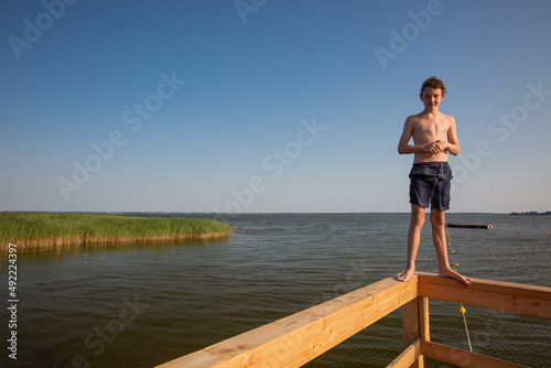 Teenage boy is standing at the parapet of a pier © arianarama