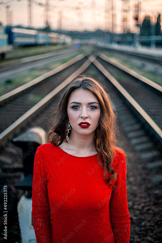 Fototapeta premium portrait beautiful young woman in a long red dress stands near the railway