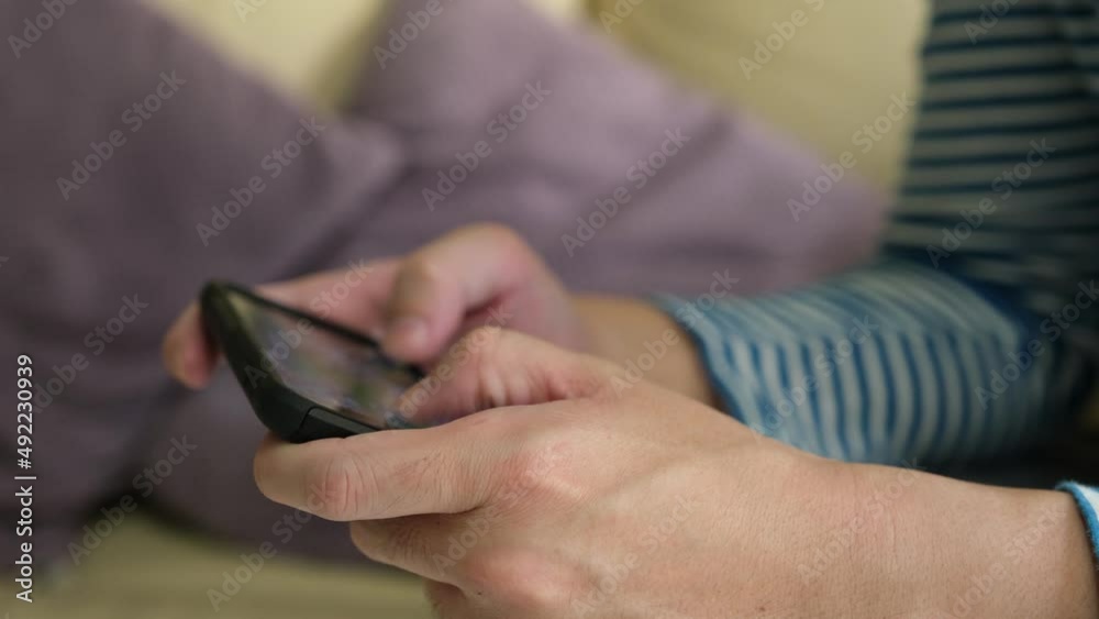 Selective focus at men hand and smartphone. Young Adult Asian man holding mobile phone playing online real time game application with mobile wireless network at home Selective focus at men hand and smartphone. Young Adult Asian man holding mobile phone playing online real time game application with mobile wireless network at home
