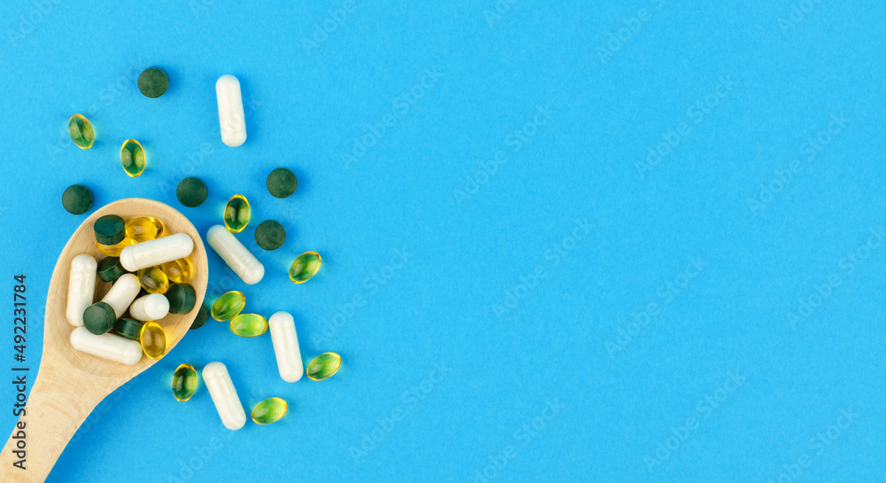 Different medical pills and capsules in a wooden spoon on a blue background