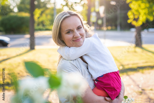 Happy mother and little daughter in the park on a sunny day at sunset. Mom and child outdoor. Concept of tenderness, family single mother, flowers, smiles, hugs, mental health, harmony, holiday