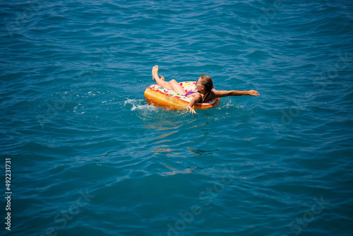 A young woman in a swimsuit swims in the sea on an inflatable donut ring. Vacation by the sea in summer
