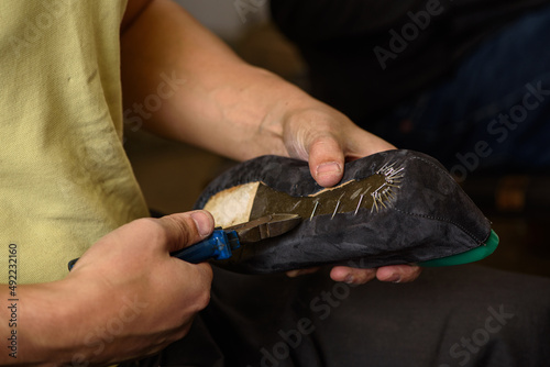 Obraz na płótnie Shoemaker making shoes sitting in workshop. Bootmaker removing nails with pliers from gray suede boot on shoe last. Closeup. w salonie