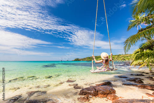 Young woman sitting on swing with beautiful tropical sea. © Nakornthai